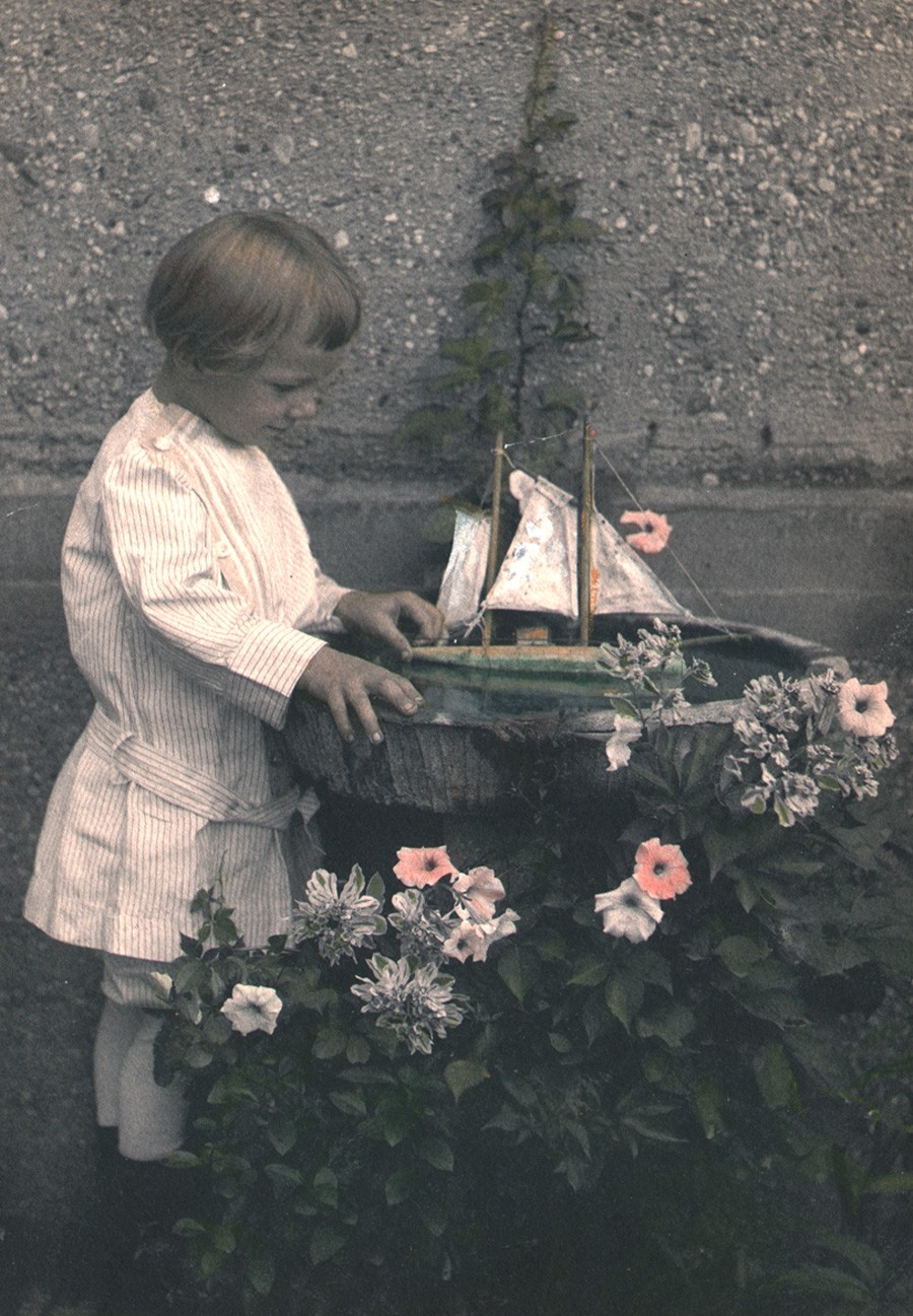 Detail: 1913: C.M. Shipman: American: his son, Mulford Cressey Shipman, (1910-1921) who died suddenly according to his obituary, plays with his toy sailboat in a birdbath: vintage platinum print with hand-coloring from memorial album: image: 21.8 x 15.2 cm: album support: 26.3 x 30.5 cm: from: PhotoSeed Archive